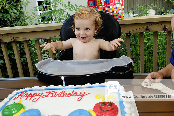 Caucasian baby boy in high chair near birthday cake