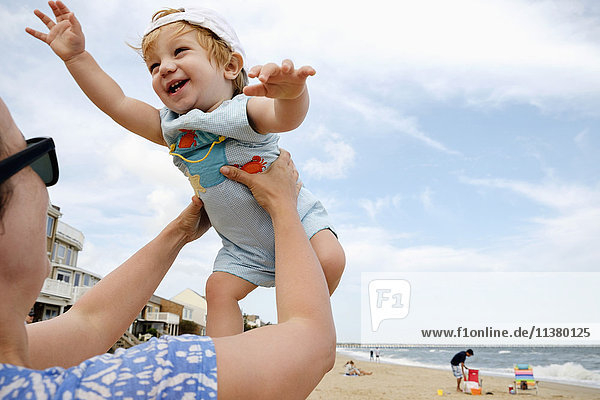 Kaukasische Mutter hebt ihren kleinen Sohn am Strand hoch