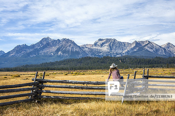 Caucasian woman sitting on wooden fence near mountain river