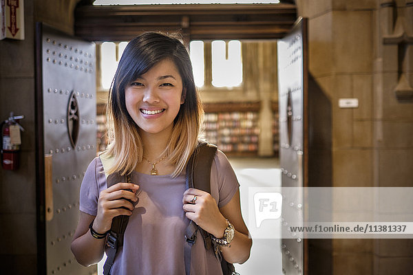 Chinesische Frau steht in der Bibliothek und trägt einen Rucksack