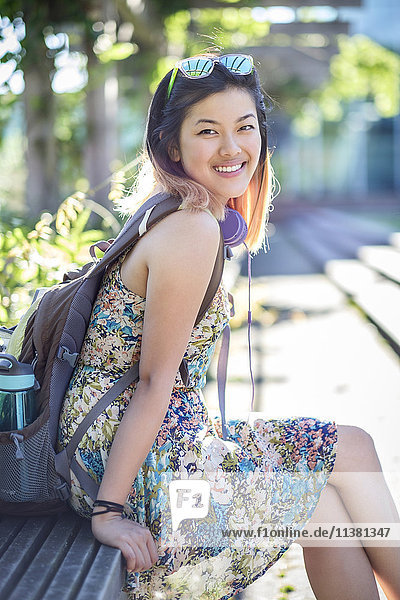 Porträt einer lächelnden chinesischen Frau auf einer Bank mit Rucksack
