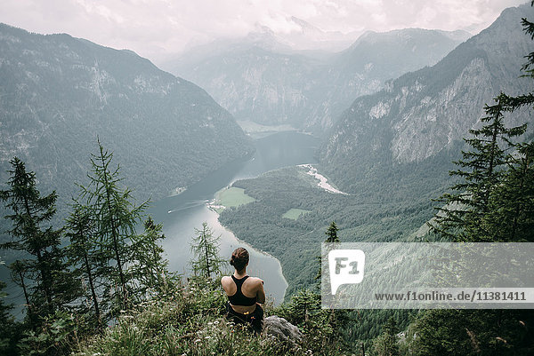Kaukasische Frau sitzt auf einem Felsen mit Blick auf einen See in einem Tal