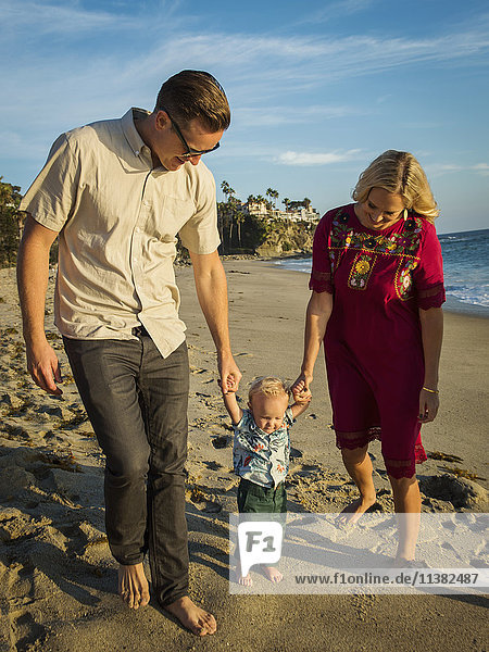 Kaukasische Mutter und Vater gehen mit ihrem kleinen Sohn am Strand spazieren