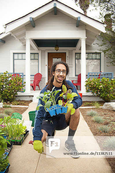 Porträt eines lächelnden schwarzen Mannes mit einem Tablett voller Pflanzen in der Nähe eines Hauses