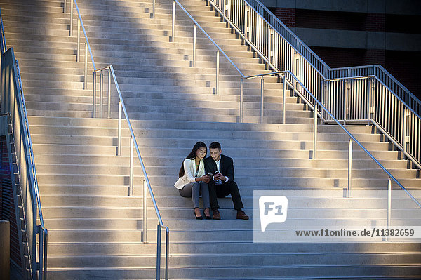 Paar sitzt auf einer Treppe und textet mit dem Handy