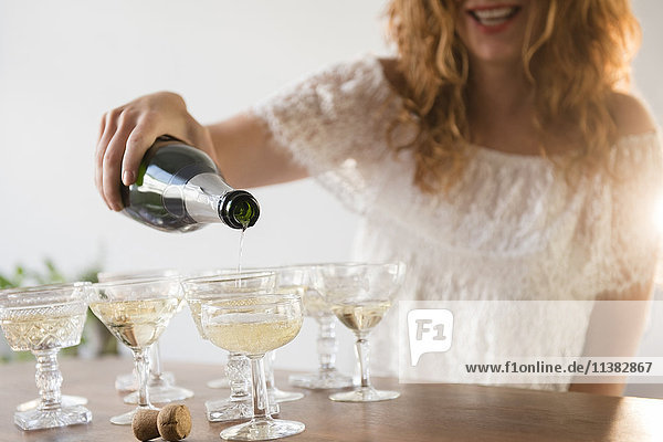 Lächelnde kaukasische Frau gießt Champagner in Coupés ein