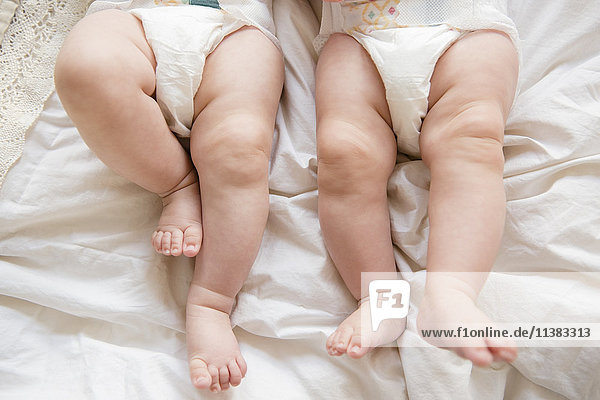 Legs of Caucasian twin baby girls laying on bed