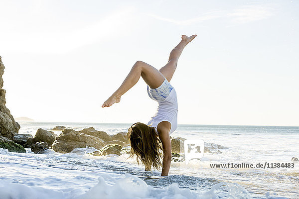 Caucasian woman doing handstand on beach