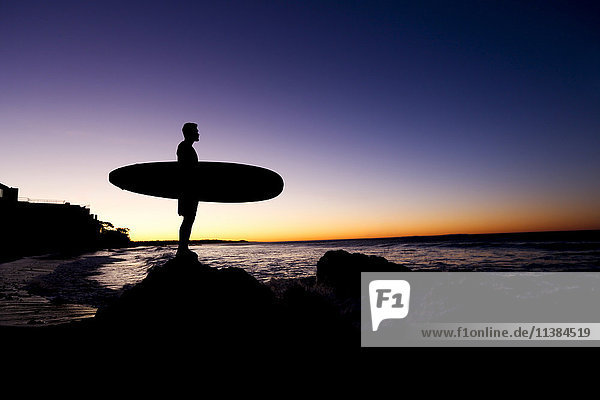 Silhouette of Hispanic man holding surfboard at beach