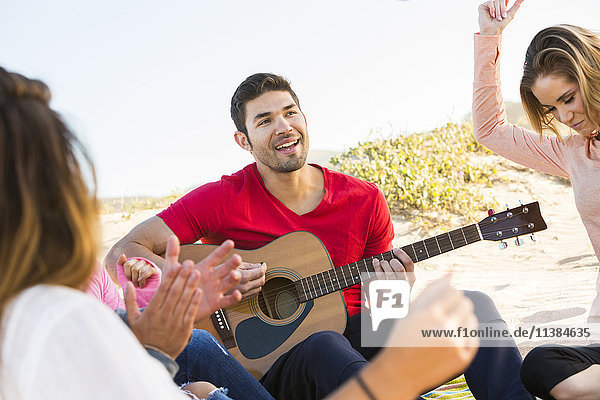 Man playing guitar for friends at beach