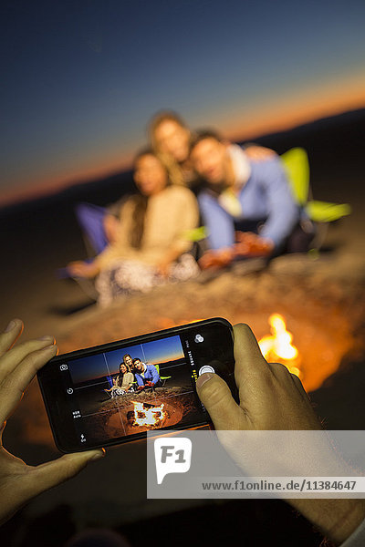 Hands of woman photographing friends on beach with cell phone