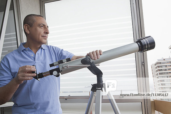 Hispanic man holding telescope near window