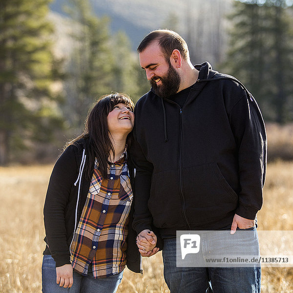 Lächelndes kaukasisches Paar hält sich auf einem Feld die Hände