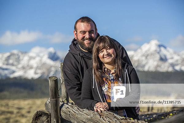 Lächelndes kaukasisches Paar lehnt sich an einen Holzzaun