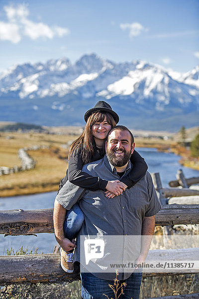 Lächelndes kaukasisches Paar posiert am Holzzaun in der Nähe des Flusses