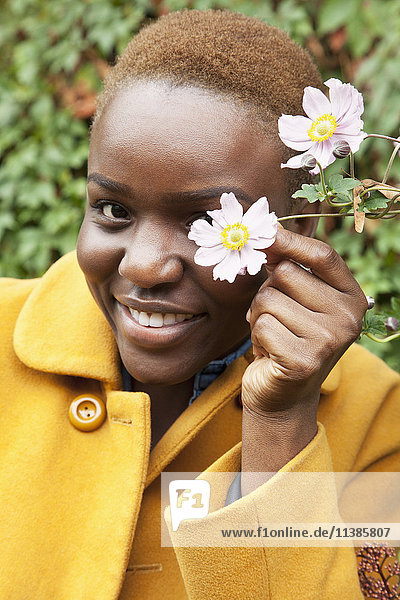 Portrait of smiling Black woman covering eye with flower