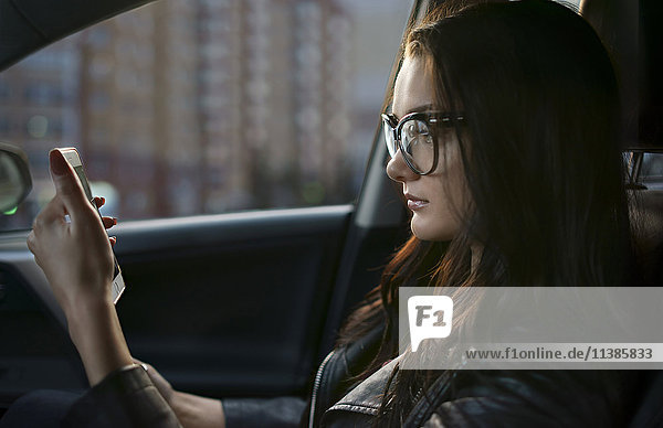Kaukasische Frau sitzt im Auto und schreibt eine SMS auf ihrem Handy