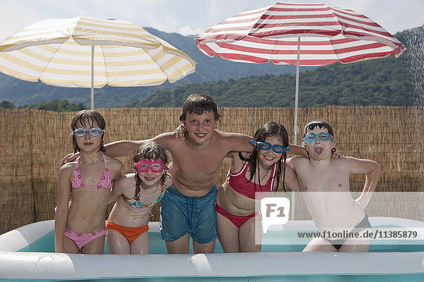 Lächelnde kaukasische Kinder posieren im aufblasbaren Schwimmbecken
