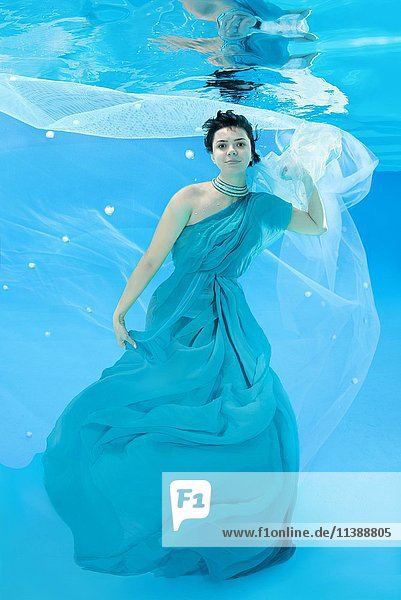 Junge Frau in langem  blauen Kleid posiert unter Wasser