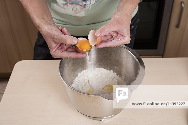 Woman puts egg in bowl of dough  baking preparation
