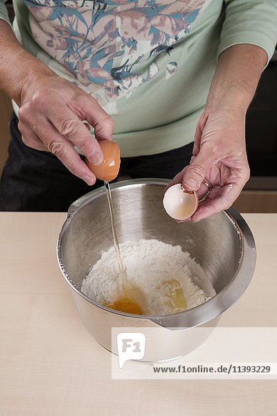 Woman putting egg in bowl of dough  Backvorbereitungen