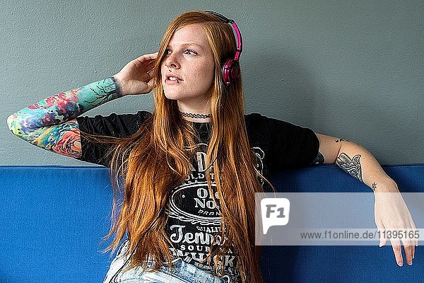 Tilburg Netherlands. Young red haired woman listening to her music uploaded on her smartphone while relaxing on her living room couch.