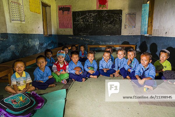 Gruppe von Kindern in blauen Kleidern  die in einem Kreis im örtlichen Kindergarten sitzen  Tatopani  Bezirk Myagdi  Nepal  Asien
