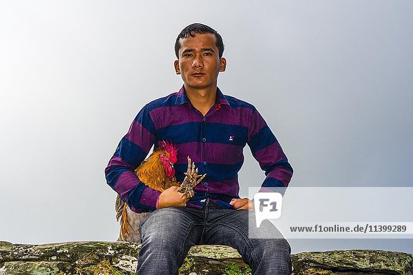 Einheimischer Mann sitzt mit einem Hahn  der bald im Khadga Devi Mandir Tempel geopfert werden soll  Darsain Hindu Festival  Bandipur  Tanahun  Nepall