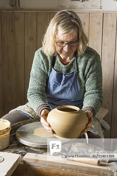 Keramische Werkstatt  Frau hebt Grundform eines Topfes von der Töpferscheibe  Pittenhart  Oberbayern  Deutschland  Europa
