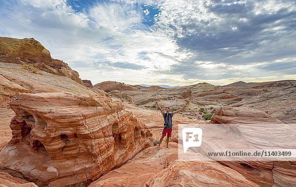Junger Mann posiert mit ausgestreckten Armen  White Dome Trail  rot-orangefarbene Felsformationen  Tal des Feuers  Mojave-Wüste  Nevada  USA  Nordamerika