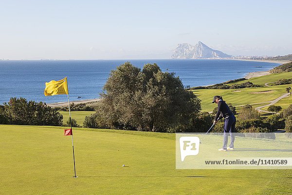 Golfer putting on green  La Alcaidesa Golf Resort with Mediterranean Sea and Rock of Gibraltar  Cádiz  Andalusia  Spain  Europe