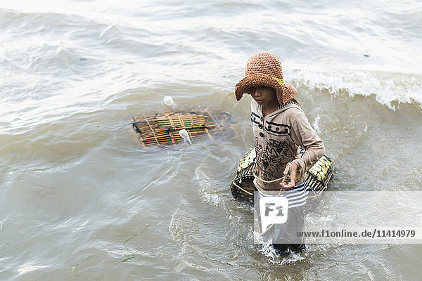 'A young woman pulls crab traps from the water  local life in the famous Crab Market; Kep  Cambodia'