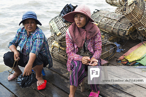 Zwei Frauen sitzen auf einem hölzernen Steg am Wasser  hinter ihnen ein Haufen Krabbenfallen  lokales Leben auf dem berühmten Krabbenmarkt; Kep  Kambodscha'.