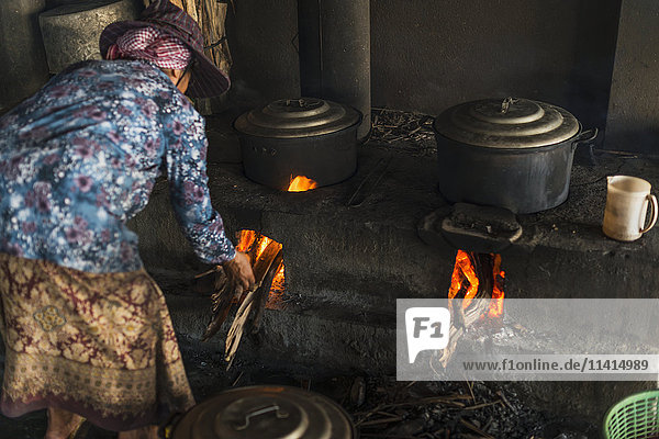 'A woman puts firewood into the flames under pots local life in the famous crab market; Kep Cambodia'