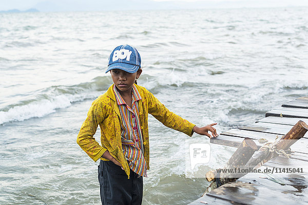 'A boy stands in the water at the edge of the dock local life in the famous crab market; Kep Cambodia'