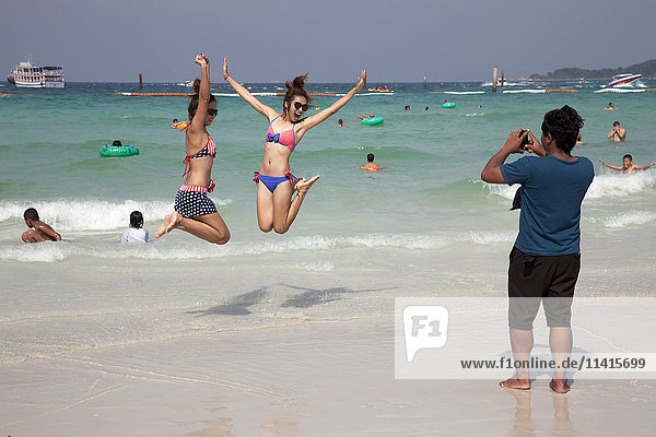 Eine Frau macht ein Foto von zwei Mädchen im Teenageralter  die beim Schwimmen am Strand in die Luft springen; Pattaya  Thailand'.