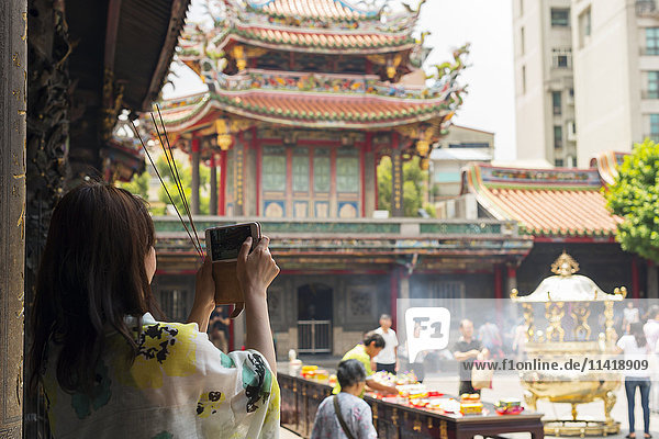'Buddhist Longshan temple in the city center of Taipei people praying and burning incense while a tourist take a picture; Taipei Taiwan China'