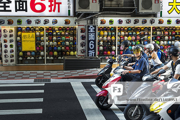 'The motorbikes and scooters in Taibei city are really a big number helmet shop in view with scooters stopped on the road; Taiwan China'