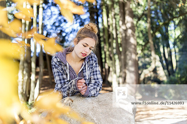Dieses junge Teenager-Mädchen sitzt allein in einem Park auf einem Felsen und denkt nachdenklich vor sich hin; New Westminster  British Columbia  Kanada.