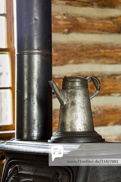 Nahaufnahme einer alten Metallkaffeekanne auf einem alten gusseisernen Ofen in einer Blockhütte mit Fenster im Hintergrund  südlich von Maple Creek; Alberta  Kanada'.