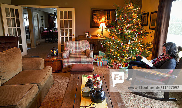 'A woman reads a Bible in her rocking chair beside a Christmas tree in her home; Chilliwack  British Columbia  Canada'