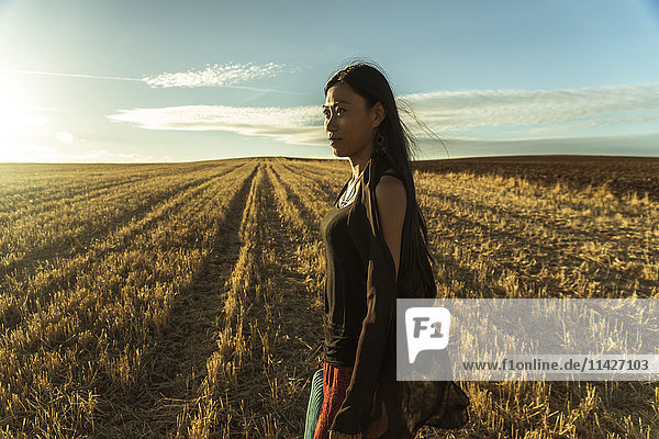 'A young Asian woman walking in a golden wheat field; Madrid  Spain'