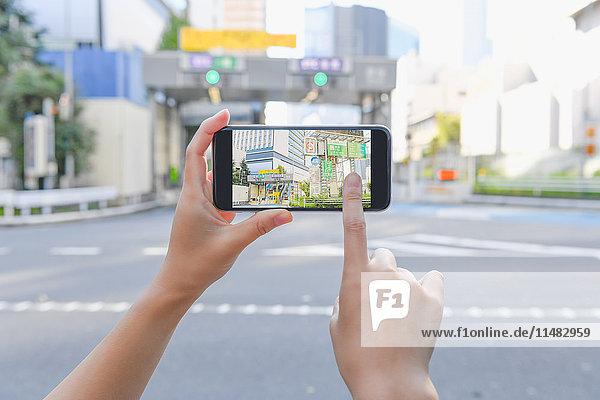 Japanische Frau  die eine Augumented-Reality-App auf ihrem Smartphone benutzt  in der Innenstadt von Tokio  Japan