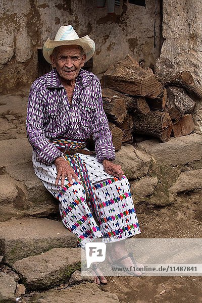 90 year old Mayan man in traditional dress sits on the rough stone steps of his home in San Pedro la Laguna  Guatemala.
