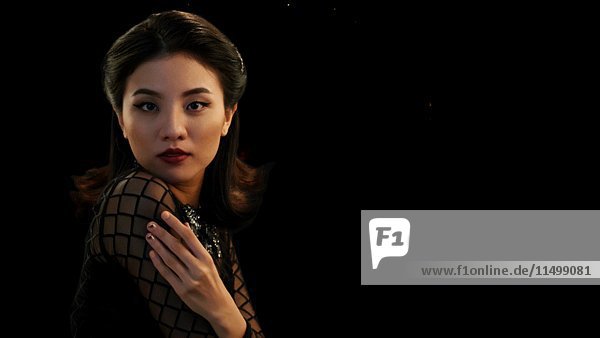 Porträt einer jungen erwachsenen asiatischen Frau im schwarzen Kleid  die mit herabfallendem Konfetti überschüttet wird
