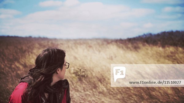 Junge erwachsene Frau im windigen Feld mit hohem Gras sitzend