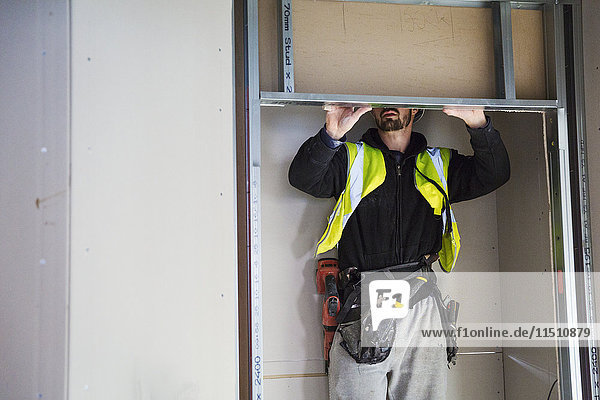 A carpenter in a small space fitting a shelf into a wall cupboard.