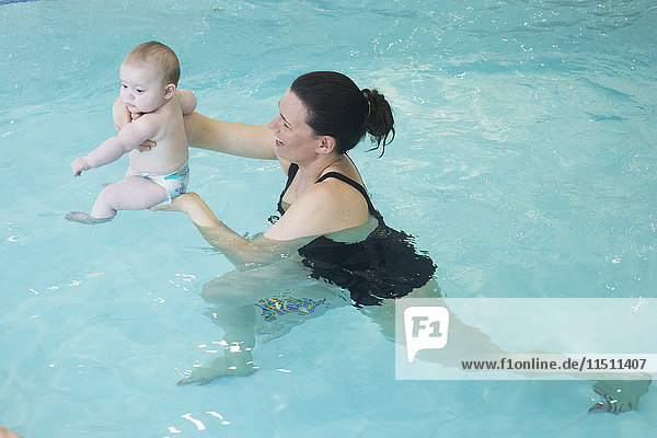 Mutter im Schwimmbad hält Kleinkind an der Wasseroberfläche
