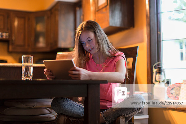 Young girl sitting crossed legged on chair using digital tablet