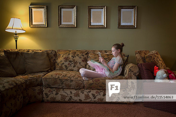 Junges Mädchen sitzend mit gekreuzten Beinen auf dem Sofa lesend
